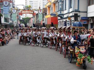 Uma multidão de pessoas vestidas tipicamente, no Oktoberfestalendário de Eventos em Blumenau: Oktoberfest, Festitália, Páscoa e Natal na Vila Germânica