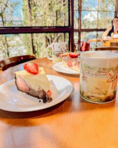Delicioso café, com uma generosa fatia de bolo de massa branca e um morango partido ao meio, no topo da fatia