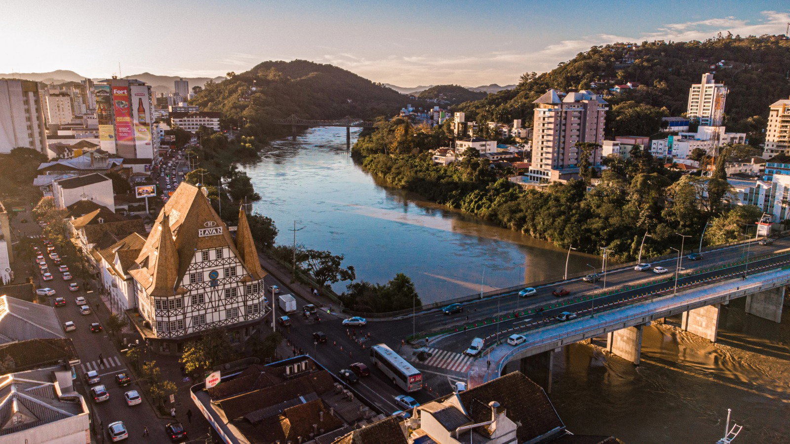 Imagem aérea de Blumenau, ao pôr do sol, com um belo rio atravessando a imagem.
